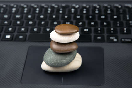 pyramid of stacked stones on the background of a laptop keyboard. stabilization and balance in lifeの写真素材