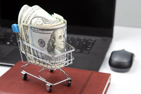Model of a grocery cart with dollar money on the background of a laptop. Online business sale. financial business success.の写真素材
