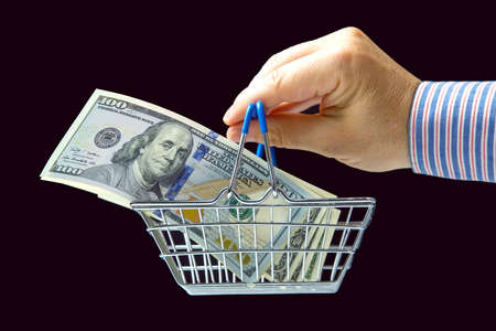 businessman hand with dollars in a grocery basket on a dark background. financial investments in...