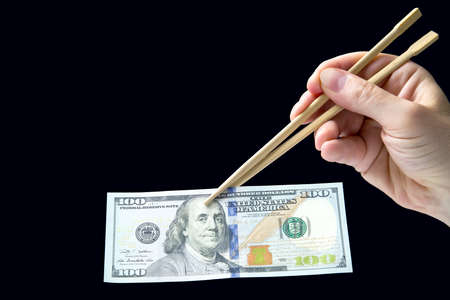 hand holds dollars with bamboo chopsticks on a dark background. financial industry in food. cash...
