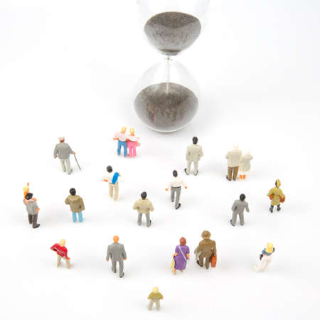 miniature people. different people are walking next to the hourglass on a white background. lifespan...
