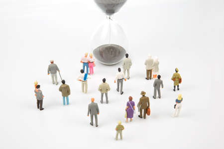 miniature people. different people are walking next to the hourglass on a white background. lifespan...