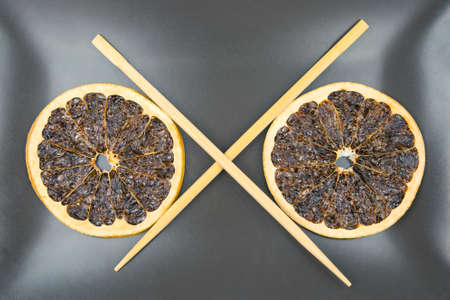 bamboo chopsticks lie on a ceramic plate with dried citrus fruits. items for foodの写真素材