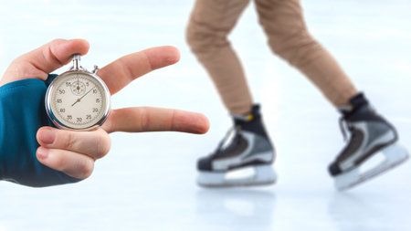 measuring speed on skates with a stopwatch. hand with a stopwatch on the background of the legs of a man skating on an ice rinkの写真素材