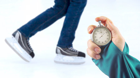 measuring speed on skates with a stopwatch. hand with a stopwatch on the background of the legs of a man skating on an ice rinkの写真素材