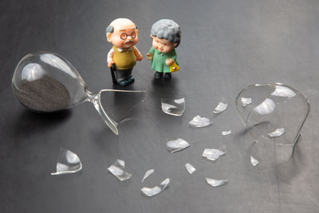 miniature people. a couple of elderly people near a broken hourglass. life time crisis. the concept of the end of life for a personの写真素材