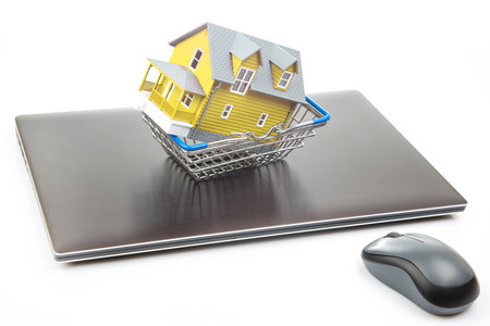 house model in a grocery cart on the background of a laptop. buying real estate online.の写真素材
