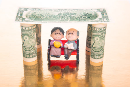 miniature people. a couple of pensioners under the house of dollars. financial security and pension for the elderly. concept of financial independenceの写真素材