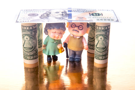 miniature people. a couple of pensioners under the house of dollars. financial security and pension for the elderly. concept of financial independenceの写真素材