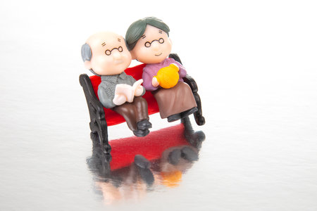 miniature people. figures for the concept. a couple of retired people are sitting together on a bench. old age and helping each otherの写真素材