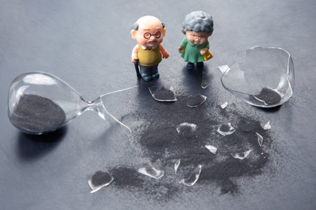miniature people. a couple of elderly people near a broken hourglass. life time crisis. the concept of the end of life for a personの写真素材