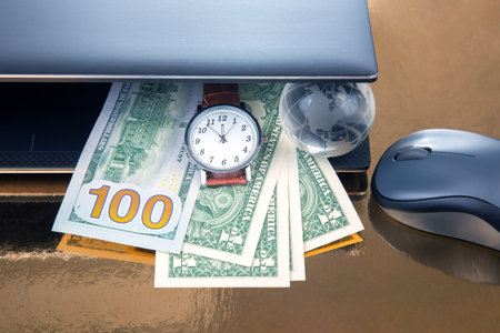 Dollars, earth globe model, wrist watch near laptop with mouse. Business online anywhere in the world. Working hours for working with a laptopの写真素材