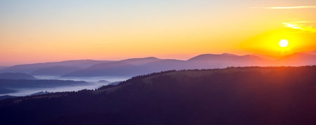 Colorful clouds in the sky at sunset against the backdrop of a mountainous forest area.の写真素材
