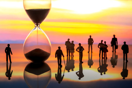 miniature people. silhouettes of different people watching the sunset next to the hourglass. end ofの写真素材