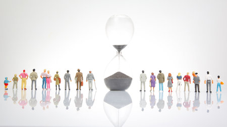 miniature people. group of different people stand near an hourglass against a white background....