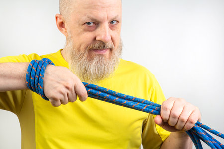 strong colored rope for climbing equipment in the hand of a bearded man in a yellow T-shirt on a light background. item for tourism and travelの写真素材