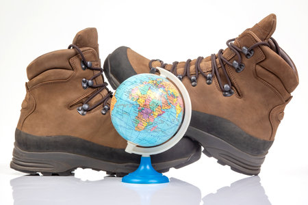 Trekking boots for hiking next to a world globe model on a white background. Equipment for travel and hikingの写真素材