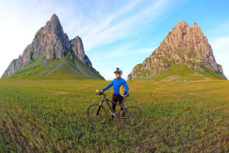 cyclist with a bicycle is resting on a green field against a blue sky. sports and recreation in...