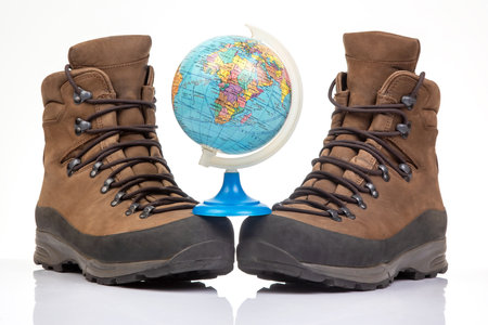 Trekking boots for hiking next to a world globe model on a white background. Equipment for travel and hikingの写真素材