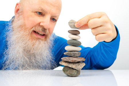 Senior man with a big smile, passionately involved in balancing various colored stones into a...