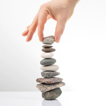 hand builds a pyramid from stacked stones on a white background. stabilization and balance in lifeの写真素材