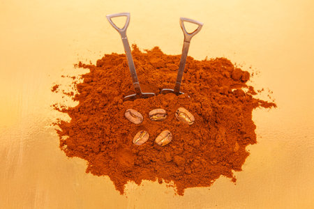 Close-up of two shovels in a pile of rich ground coffee, surrounded by whole coffee beans on a shiny...