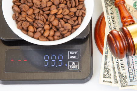 A striking arrangement featuring a digital scale bearing a bowl of coffee beans, complemented by money and a gavel, symbolizing the intersection of commerce, law, and agriculture.の写真素材