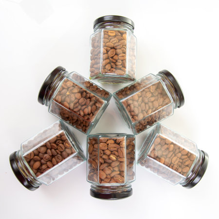 six glass jars with black lids filled with roasted coffee beans on a white backgroundの写真素材