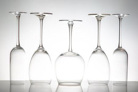 Five crystal-clear wine glasses with varied shapes stand in a row, their reflections shimmering on a...