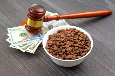 A courtroom gavel rests on US currency with coffee beans in a bowl, on a wooden surface, depicting the intersection of law, money, and trade.の写真素材