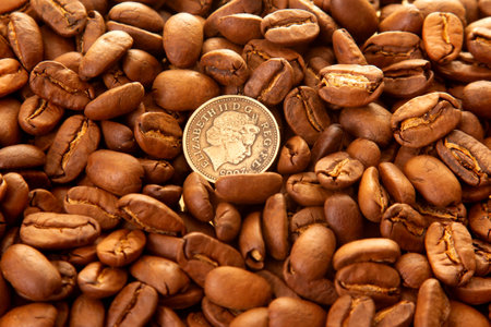 Close-up of roasted coffee beans surrounding a dime on a shiny gold surface, highlighting their...