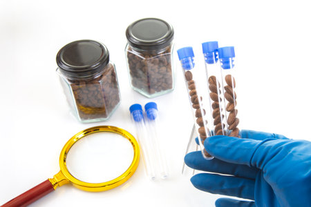 A gloved hand holds test tubes with coffee beans, surrounded by jars, a magnifying glass, and...