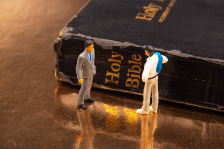 Two miniature figurines, one in a suit and one in casual attire, standing on a golden surface beside...