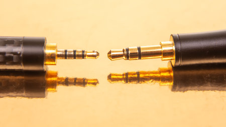 Close-up of two 3.5mm audio jacks with gold connectors on a reflective golden surface, ideal for...