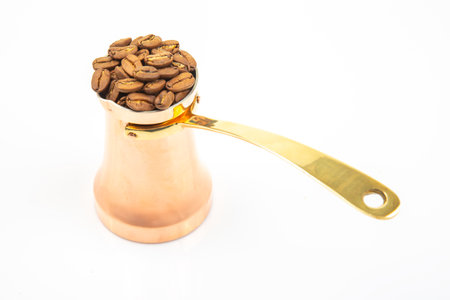 Handcrafted copper cezve with a long brass handle paired with roasted coffee beans on a white backdrop, perfect for coffee preparation and rustic decor images.の写真素材