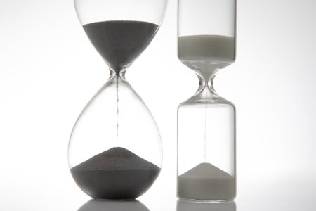 A sleek hourglass with dark sand flowing against a stark white background, symbolizing time. Ideal for minimalist, time-related themesの写真素材