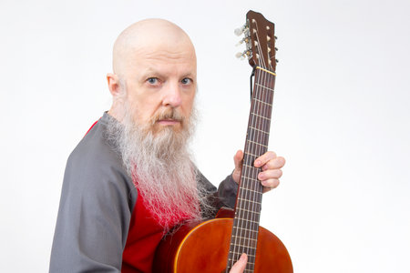 Bald senior with a flowing white beard strums an acoustic guitar, in a red and gray shirt, isolated on white, depicting a moment of musical expression and creativity.の写真素材