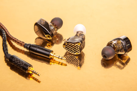 Three earbuds with braided cables and 3.5mm plugs on a gold surface, great for showcasing audio accessories and tech equipment.の写真素材