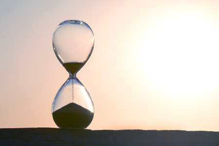 Hourglass framed by a radiant sunset, sand trickling down in soft light. Great for illustrating...