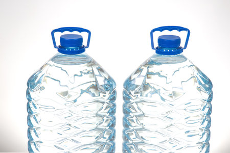 Two transparent water bottles with blue caps and a textured pattern, placed on a white surface. Great for promoting hydration, healthy living, or sustainable lifestyle concepts.の写真素材