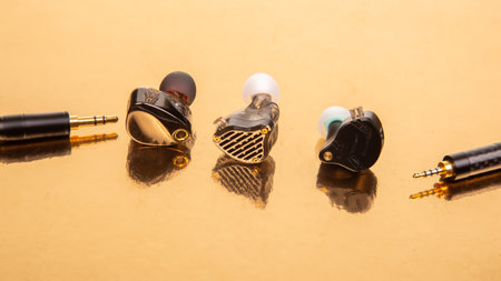 Elegant trio of wired earbuds with braided cables and gold-plated 3.5mm plugs on a shiny gold backdrop, suitable for tech, audio, and modern design photography.の写真素材