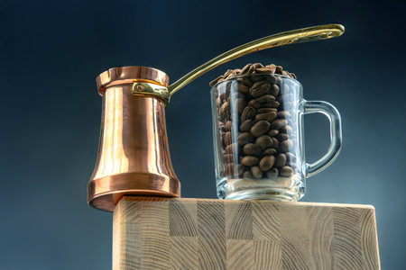 A vintage-style cezve with a golden handle and a glass cup filled with coffee beans rest on a wooden cutting board. A refined still-life celebrating coffee culture and tradition.の写真素材