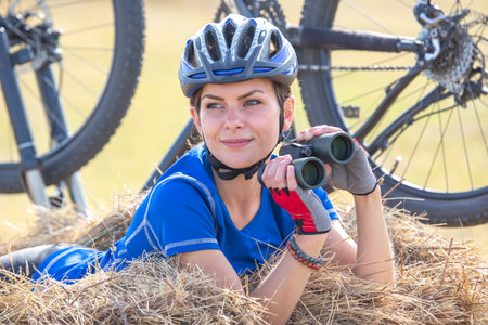 Beautiful woman cyclist with binoculars in hand on the background of the bike.