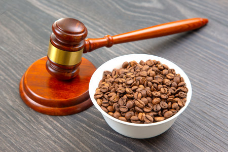 A wooden gavel with a gold band rests beside a pile of roasted coffee beans on a dark wooden surface, blending justice and coffee themes for unique legal or cafÃ© visuals.の写真素材