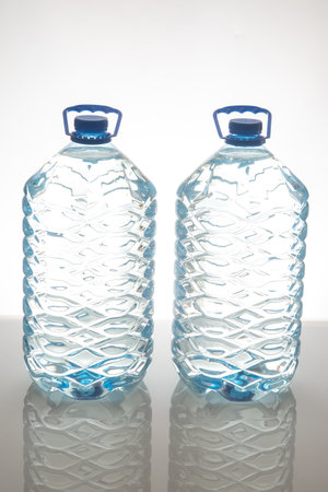 Two large plastic water bottles with blue caps and textured design, standing side by side on a white...
