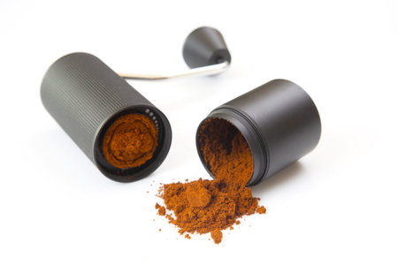A modern manual coffee grinder, opened to show ground coffee, with some powder spilled on a white background, ideal for kitchen and coffee-related stock photography.の写真素材