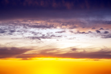 Dramatic sunset sky featuring golden, fiery clouds against a deepening blue background. The rich colors and dynamic cloud formations create a stunning natural display.の写真素材