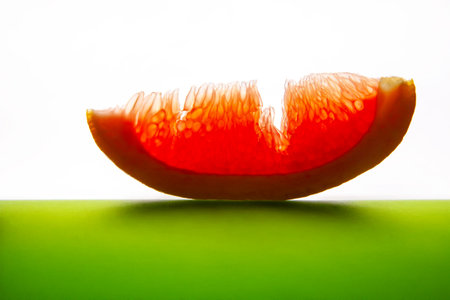 A vibrant half grapefruit with juicy red flesh, sliced and placed on a reflective green surface against a white background, showing freshness and texture. Perfect for food and health themes.の写真素材