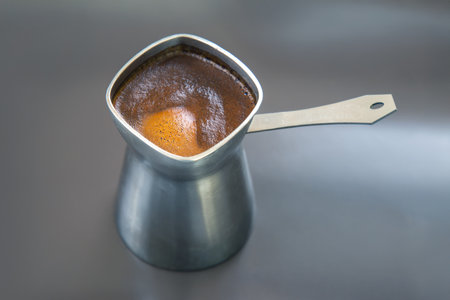 Elegant image of a metal cezve with frothy Turkish coffee on a gray backdrop. Suitable for coffee shop branding, food photography, or cultural beverage visuals.の写真素材