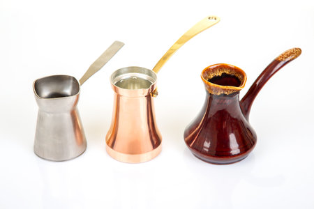 Collection of Turkish coffee makers in metallic silver, glossy red ceramic, and shiny copper with gold handles, displayed on a white surface, great for coffee lover and cultural heritage visualsの写真素材